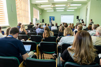 Audience from the back with one speaker and screen showing a presentation. 
