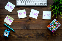 Desk with a laptop, writing tools and notes showing times such as 9:00.