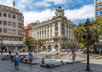 People enjoying a sunny day at a fountain on Knez Mihailova Street in Belgrade, surrounded by historic buildings.